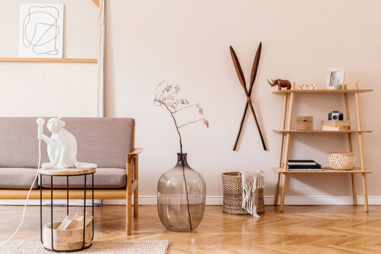Stylish interior design of living room at cozy apartment with brown sofa, coffee table with lamp, bookstand, vase and elegant accessories. Minimalistic concept of home staging Beige wall. Template.