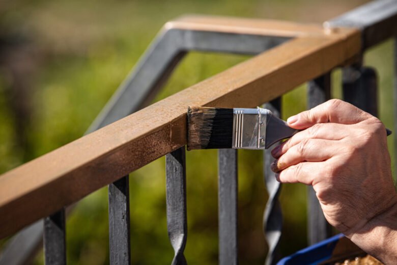 man is painting a metal railing with copper varnish