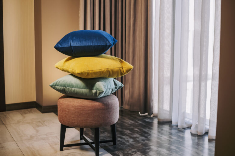 Pile of colorful pillows on padded stool next to the windows. Interior design elements with pillows