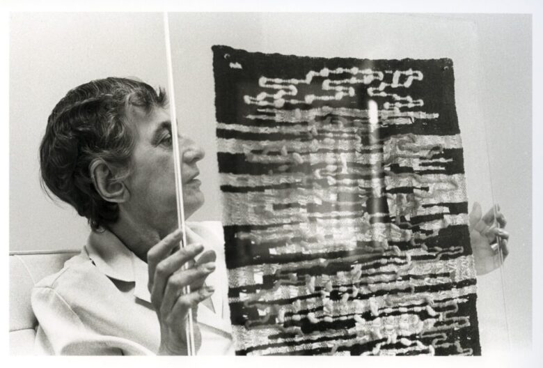 12_PS_DEDAR_WEAVING ANNI ALBERS_Anni Albers holding her weaving Under Way, New Haven, Connecticut, ca. 1965_Photograph by John T. Hill_Image courtesy of the Josef and Anni Albers Foundation