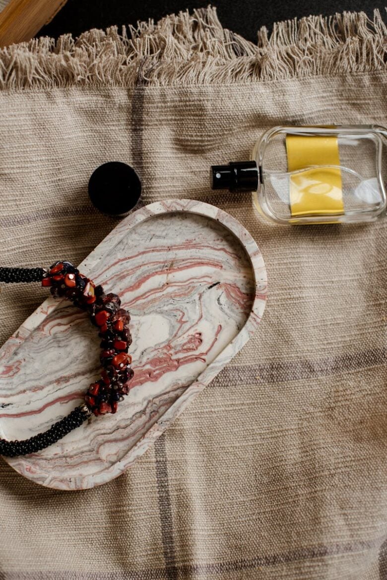 A stylish display of a marble tray with jewelry and a clear perfume bottle on rustic fabric.