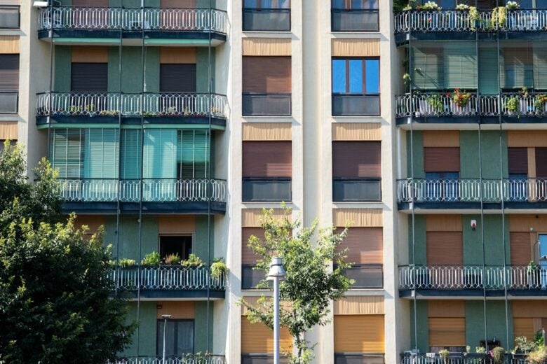 Contemporary apartment facade with glass balconies and green accents, capturing urban residential life.