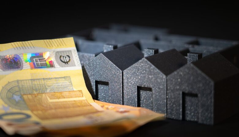 Close-up of black miniature houses with Euro notes, representing real estate investment and savings.