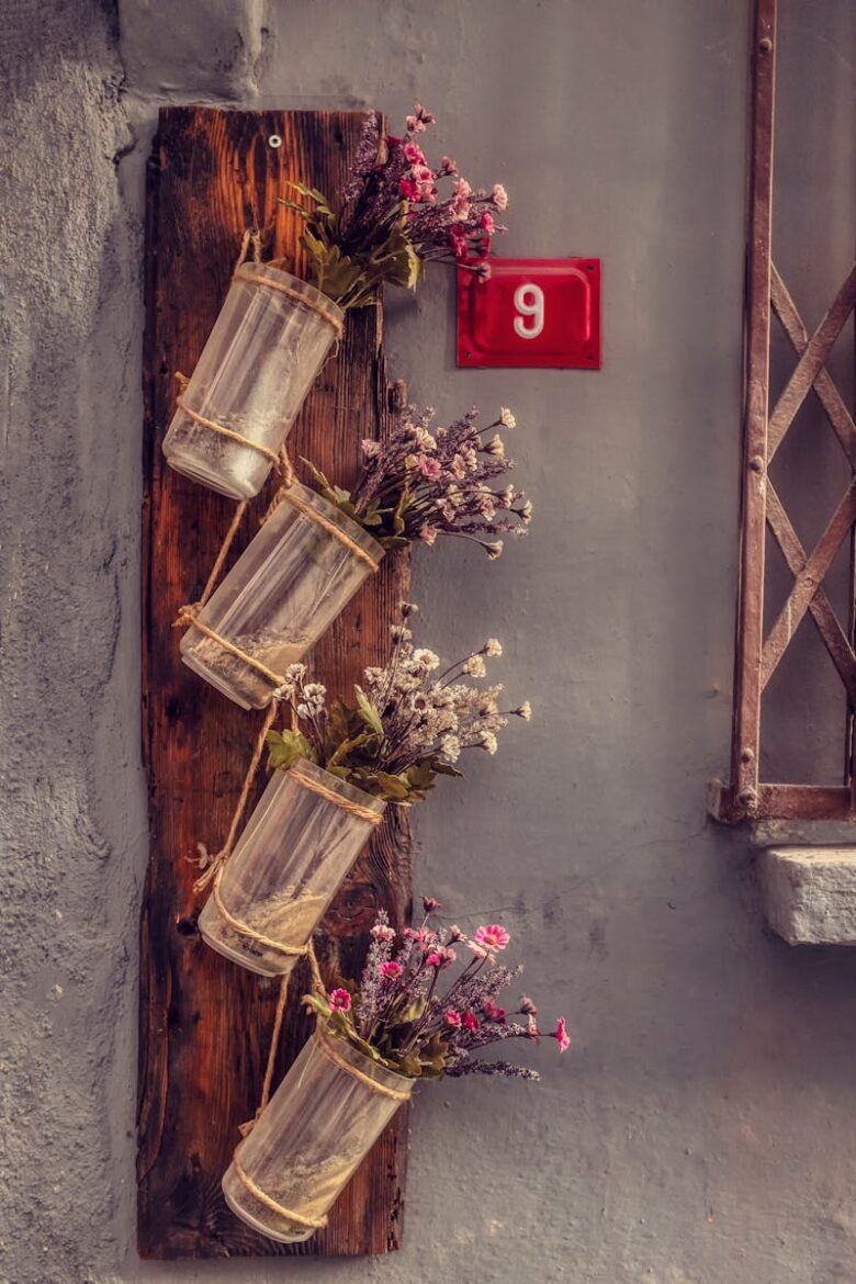 Vertical wooden board with glass jars and flowers on a gray wall. Number 9 sign adds charm.