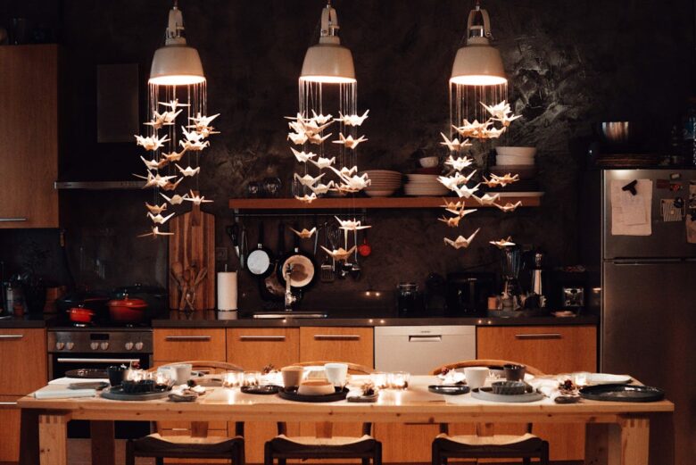 Table setting with dishware placed near kitchenware and contemporary appliances decorated with hanging paper cranes in modern kitchen at home