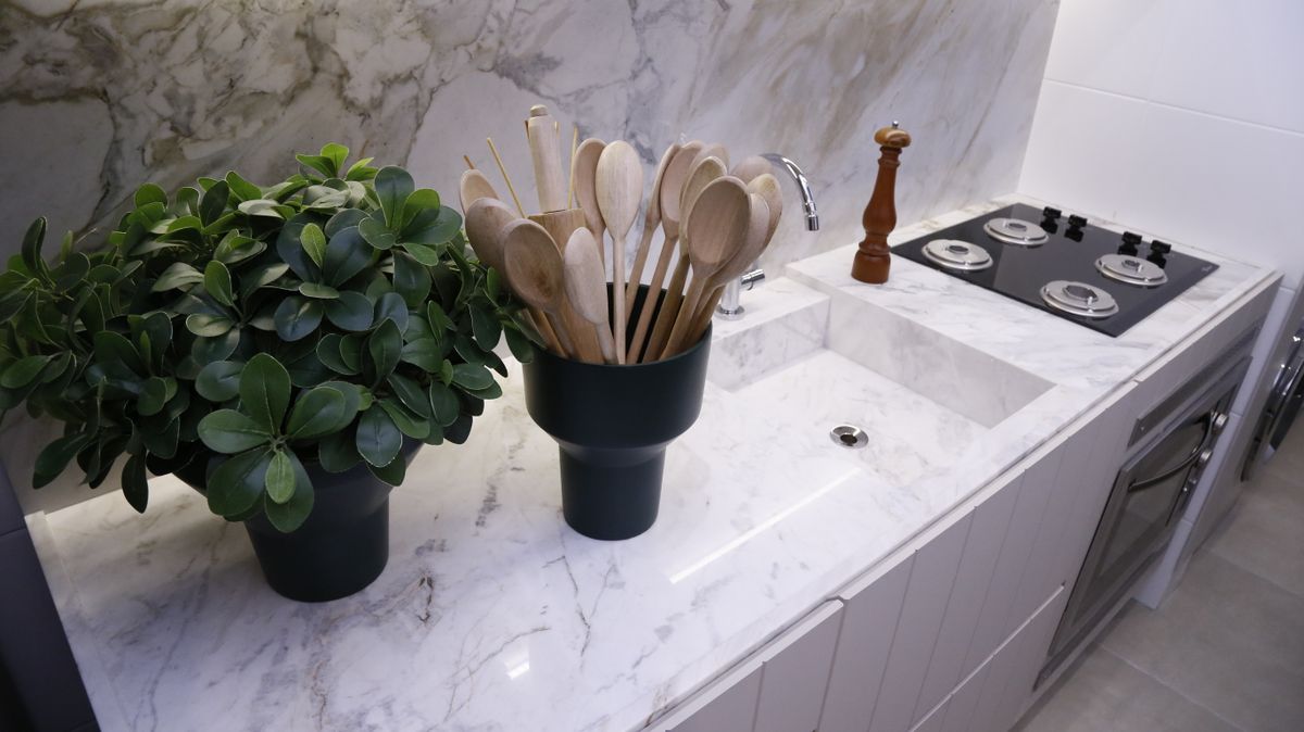 Sleek minimalist kitchen with marble counter, wooden spoons, potted plant, modern fixtures, and stovetop. Sleek minimalist kitchen with marble counter, wooden spoons, potted plant, modern fixtures, and stovetop.