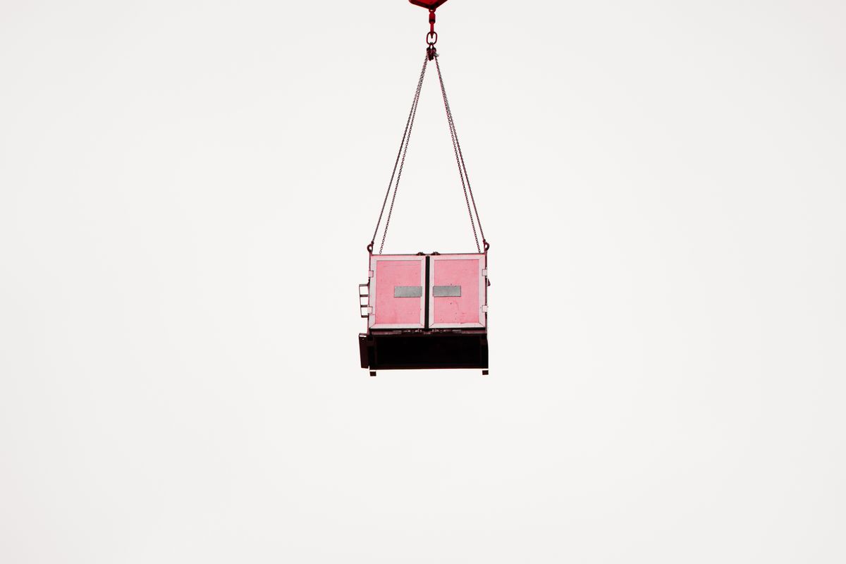 A pink cargo container suspended mid-air against a clear white sky, minimalist composition. A pink cargo container suspended mid-air against a clear white sky, minimalist composition.