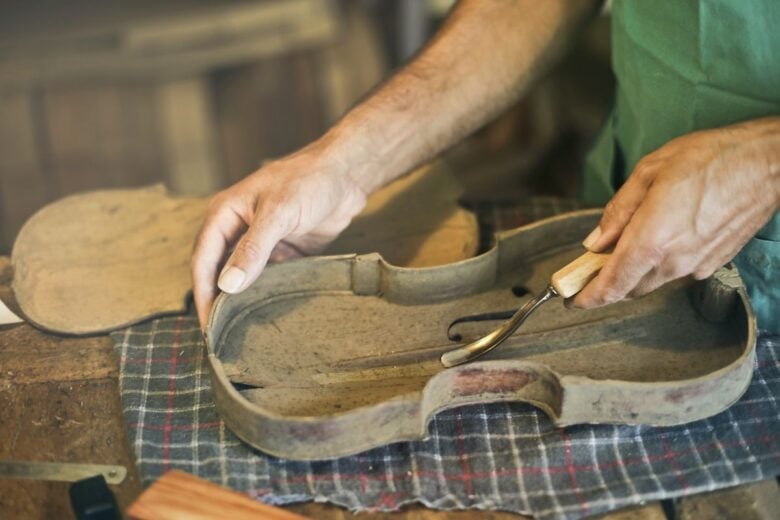Skilled artisan crafting a violin with detailed handwork on a workbench indoors.
