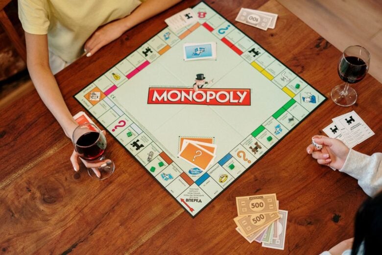 Overhead view of people playing Monopoly board game, enjoying drinks and having fun indoors.