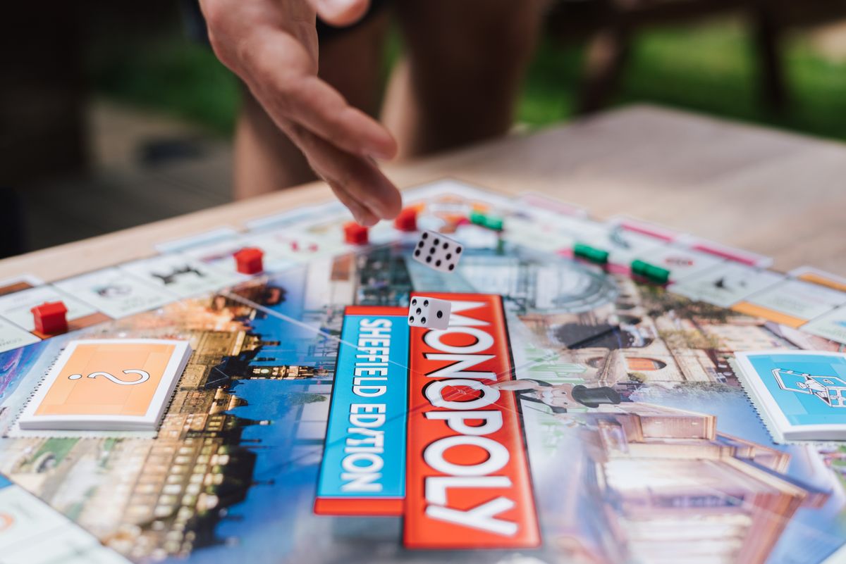Crop unrecognizable man rolling dices while playing board game at table with cards in garden Crop unrecognizable man rolling dices while playing board game at table with cards in garden