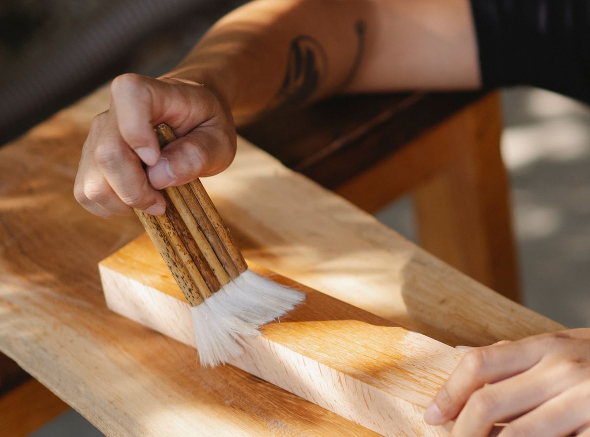 High angle of unrecognizable artisan using brush for varnishing wooden beam while working in professional workshop High angle of unrecognizable artisan using brush for varnishing wooden beam while working in professional workshop