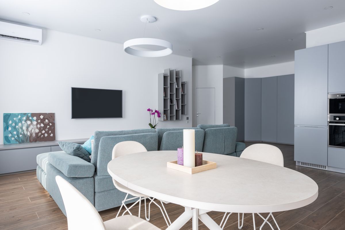 Modern interior of comfortable open plan kitchen and living room with gray sofa and TV with gray shelves hanging on wall Modern interior of comfortable open plan kitchen and living room with gray sofa and TV with gray shelves hanging on wall