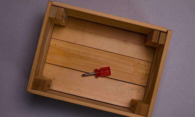 Flat lay of a wooden box with a red screwdriver placed inside on a neutral surface.