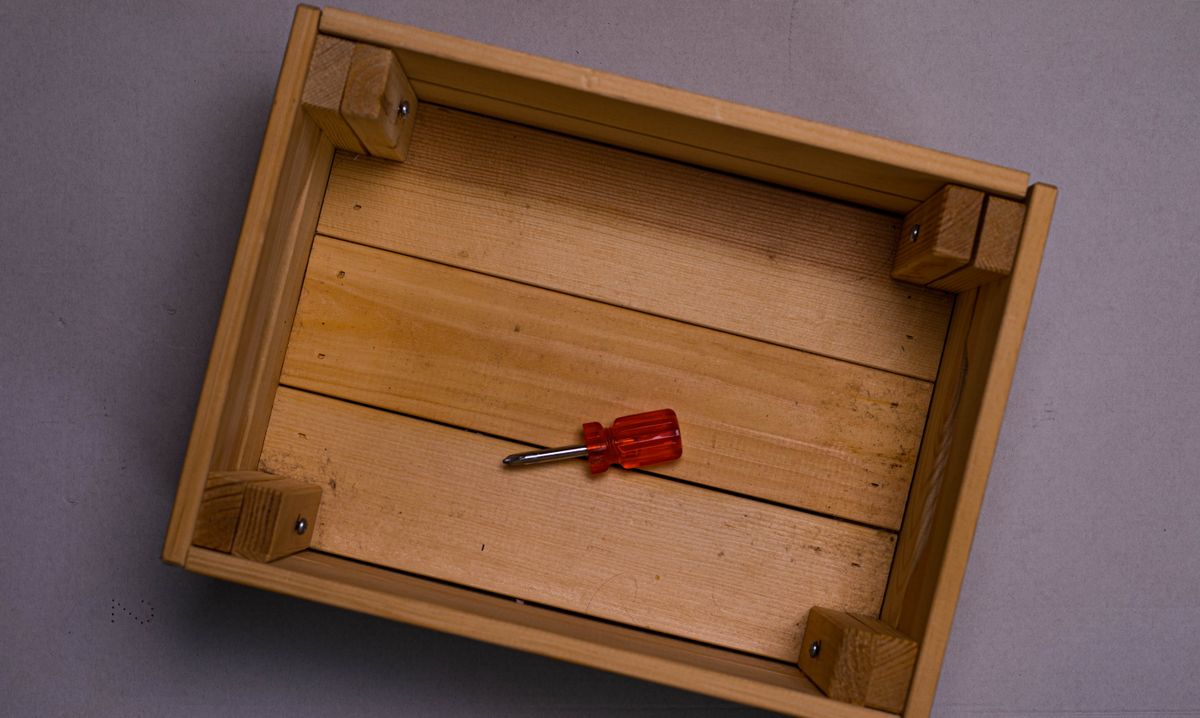 Flat lay of a wooden box with a red screwdriver placed inside on a neutral surface. Flat lay of a wooden box with a red screwdriver placed inside on a neutral surface.