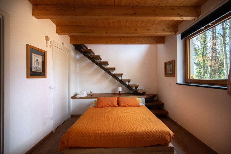 Inviting bedroom featuring an orange bedspread, modern staircase, and large window with forest view.