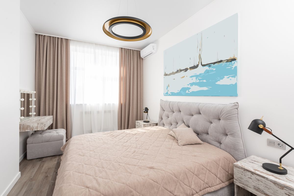 Modern bedroom interior with bed and bedside tables with lamps and pouf next to mirror and window with curtains Modern bedroom interior with bed and bedside tables with lamps and pouf next to mirror and window with curtains