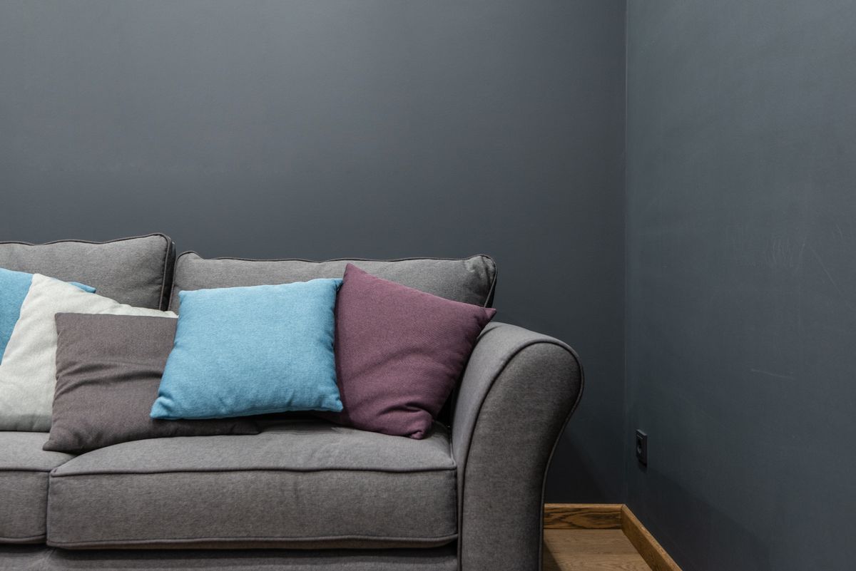 Part of soft modern gray sofa with armrest and abundance of bright pillows placed near wall in light room at home Part of soft modern gray sofa with armrest and abundance of bright pillows placed near wall in light room at home