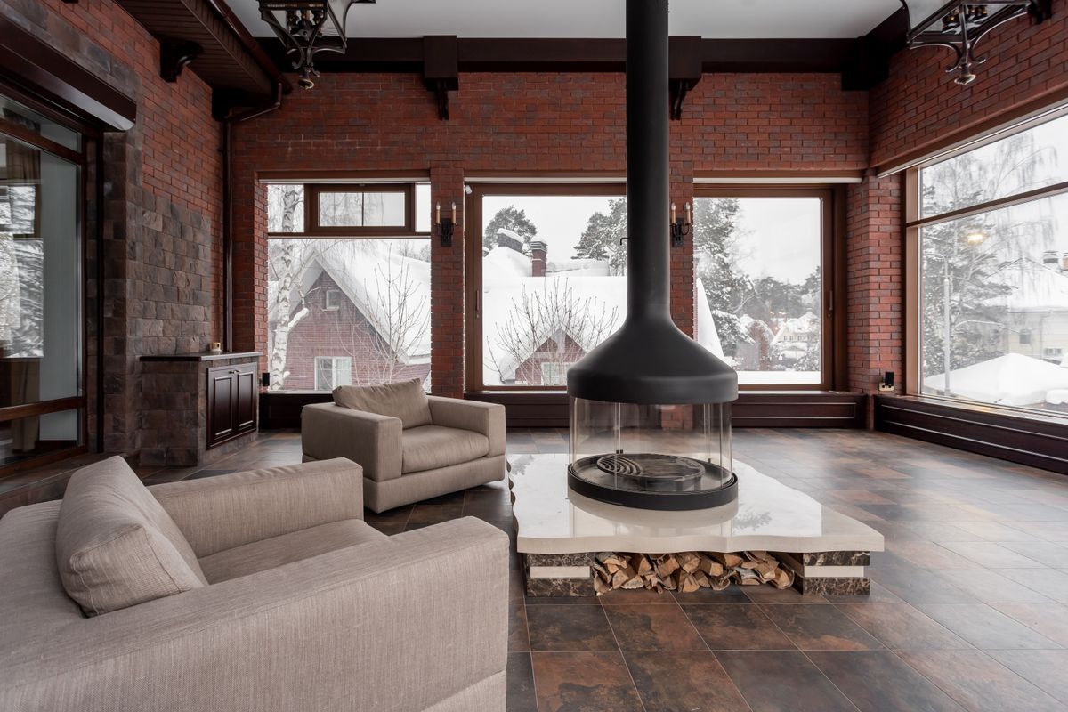 A contemporary living room with a fireplace and large windows overlooking a snowy landscape.