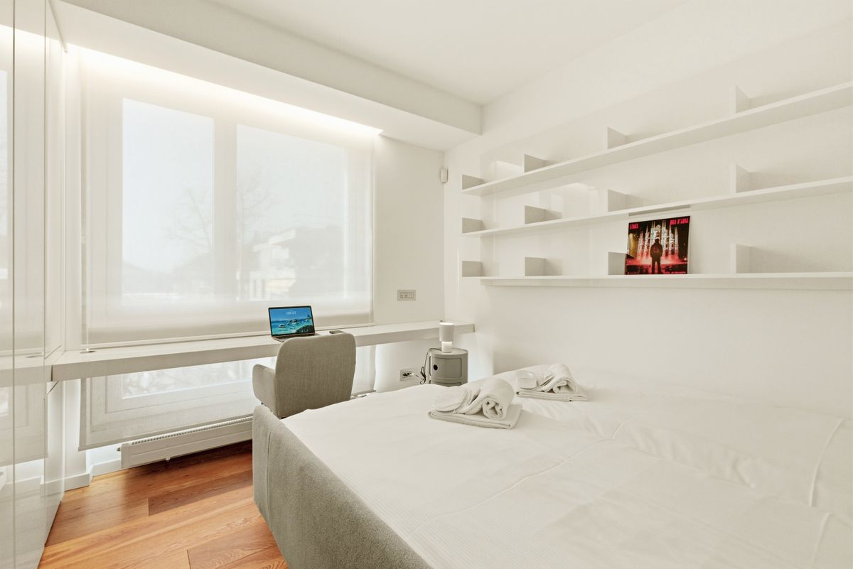 Bright modern minimalist bedroom with a desk, laptop, and clean decor.