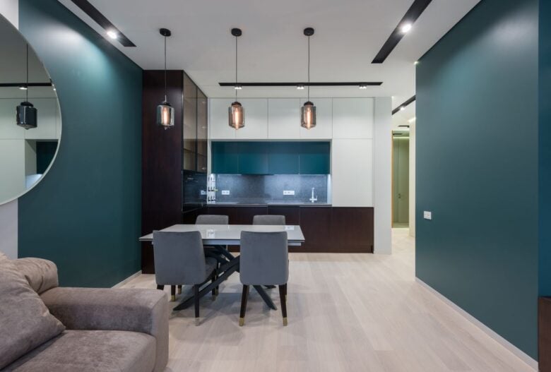 Dining table with chairs in kitchen near comfy sofa in modern studio apartment with creative design