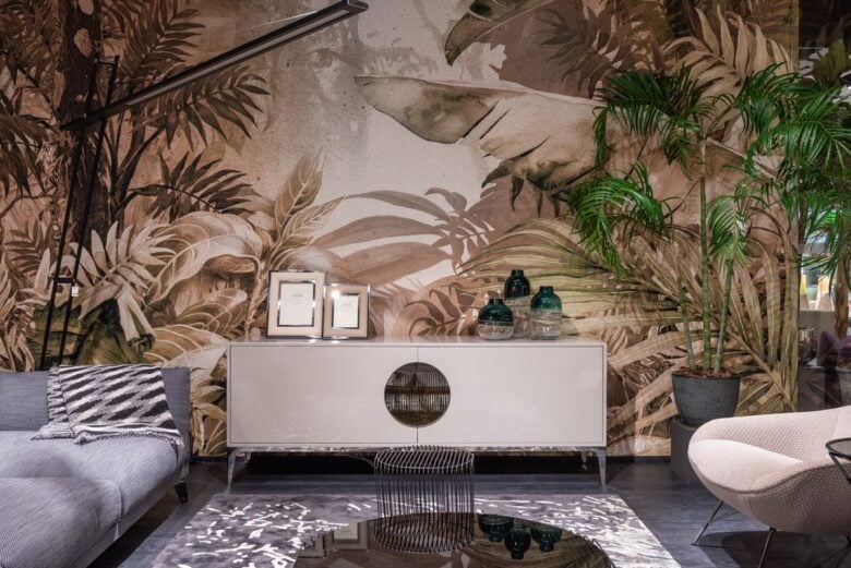 Cupboards with decorations placed on rug at painted wall between couch and armchair in contemporary shopping center with green plants