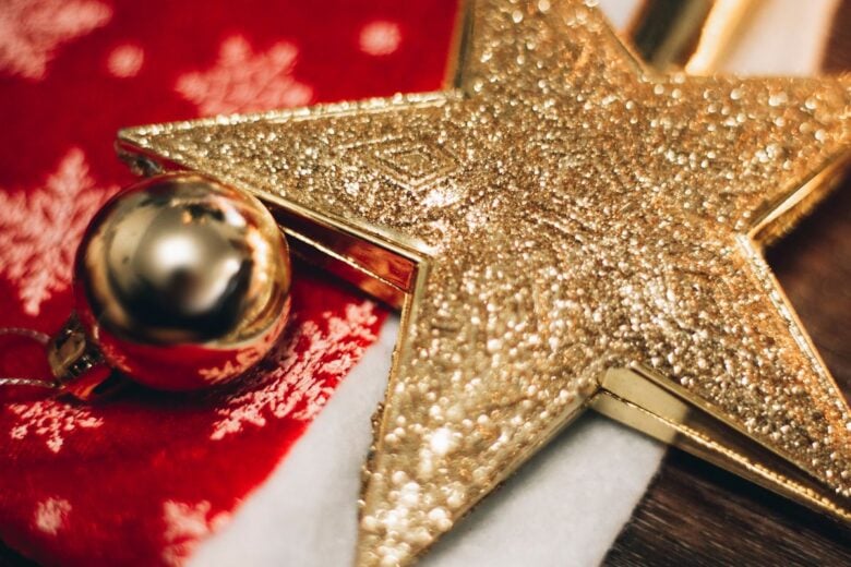 Festive close-up of a glittery golden star and bauble ornament on a red background.