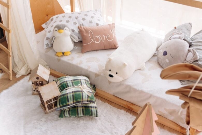 A cozy children's bedroom featuring plush animal toys, decorative pillows, and a small wooden house decor.