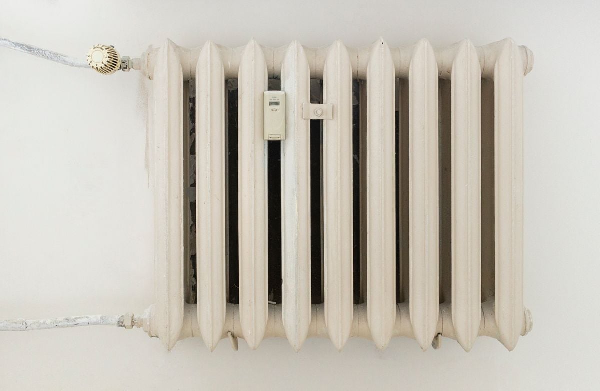 A classic white metal radiator on a plain wall, showcasing minimalist interior design. A classic white metal radiator on a plain wall, showcasing minimalist interior design.