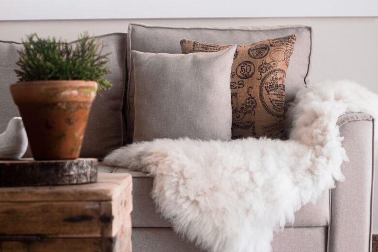 Warm and inviting living room with a focus on soft textures, featuring a sofa with fur throws and decorative pillows.