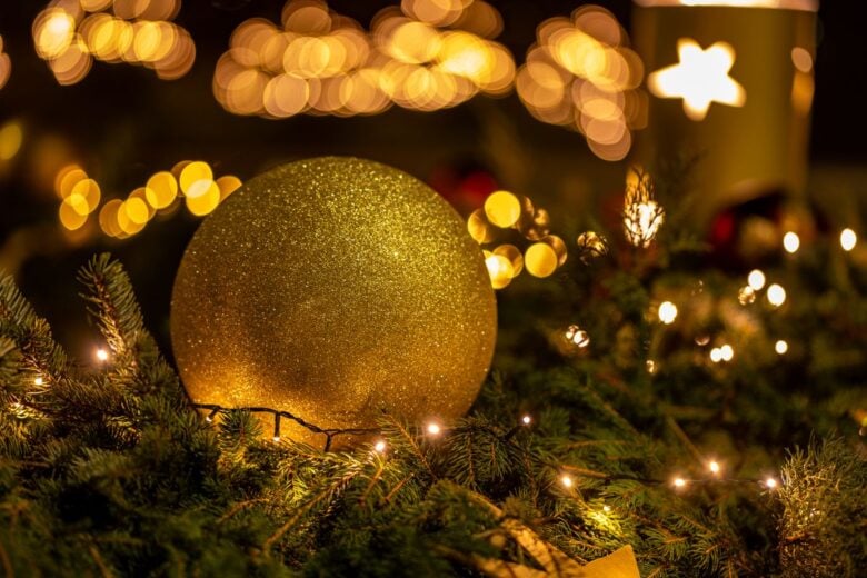 Bright gold Christmas ornament with festive lights on pine branches, evoking holiday warmth.
