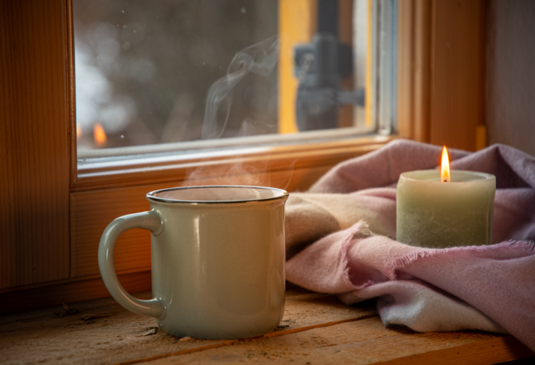 A warm cup of coffee and a candle create a cozy ambiance by the window.