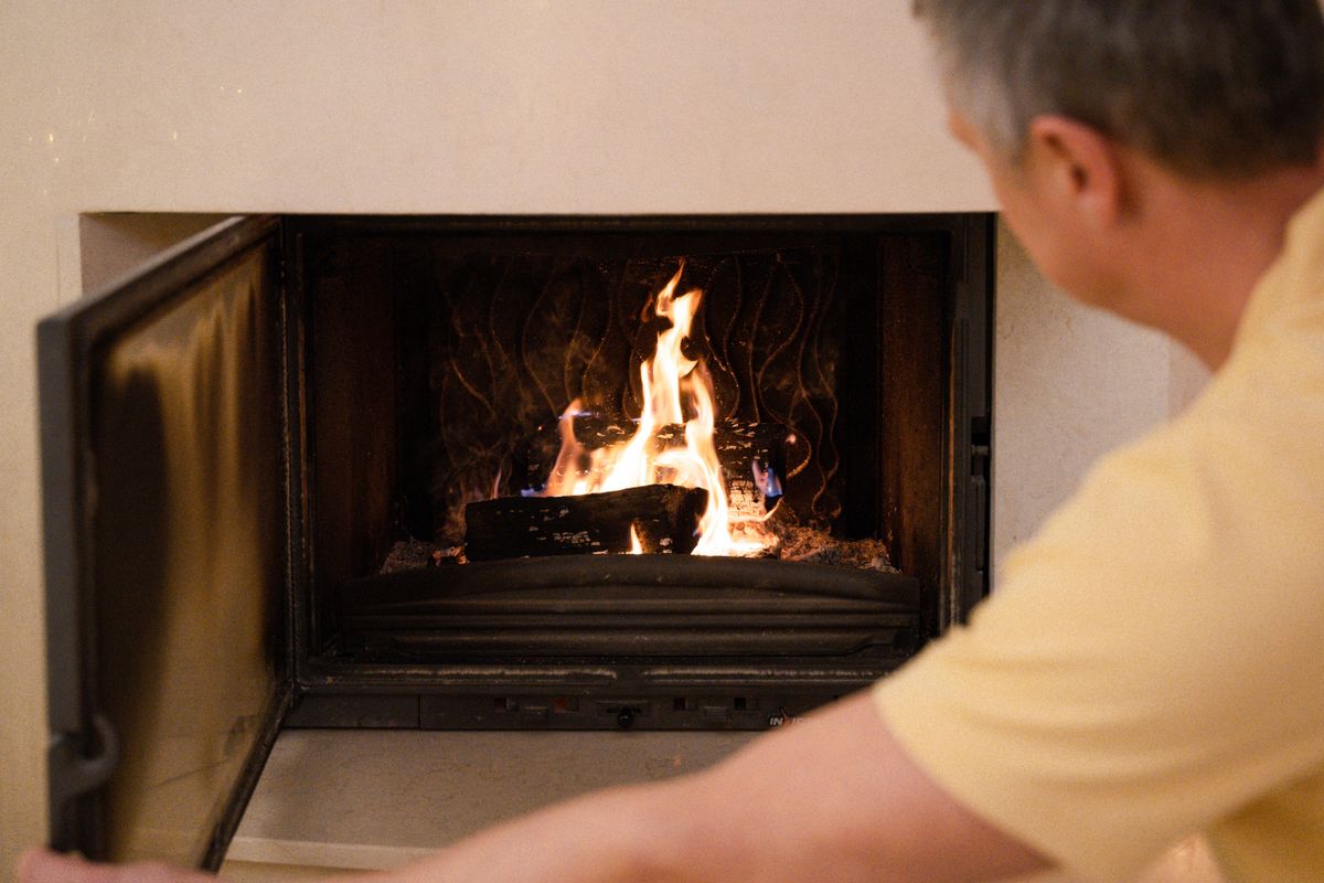 A man in a yellow shirt tends to the burning fire in a cozy indoor fireplace. A man in a yellow shirt tends to the burning fire in a cozy indoor fireplace.