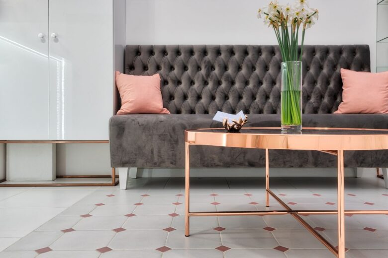 Comfortable sofa with cushions placed near round table decorated with bunch of daffodils in glass vase at reception hall