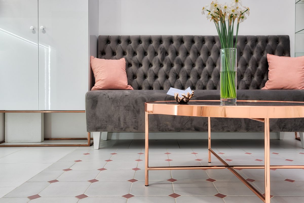 Comfortable sofa with cushions placed near round table decorated with bunch of daffodils in glass vase at reception hall