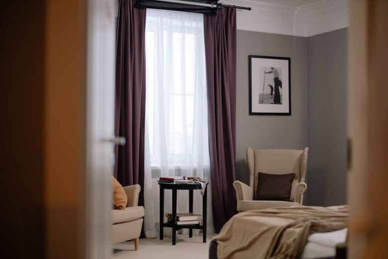 Elegant bedroom interior with armchairs, purple curtains, and a framed photo.