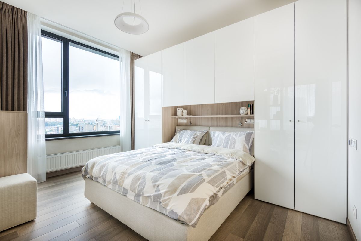 Interior of modern bedroom with white built in wall wardrobe and shelf above cozy bed with pillows and soft blanket in daylight Interior of modern bedroom with white built in wall wardrobe and shelf above cozy bed with pillows and soft blanket in daylight
