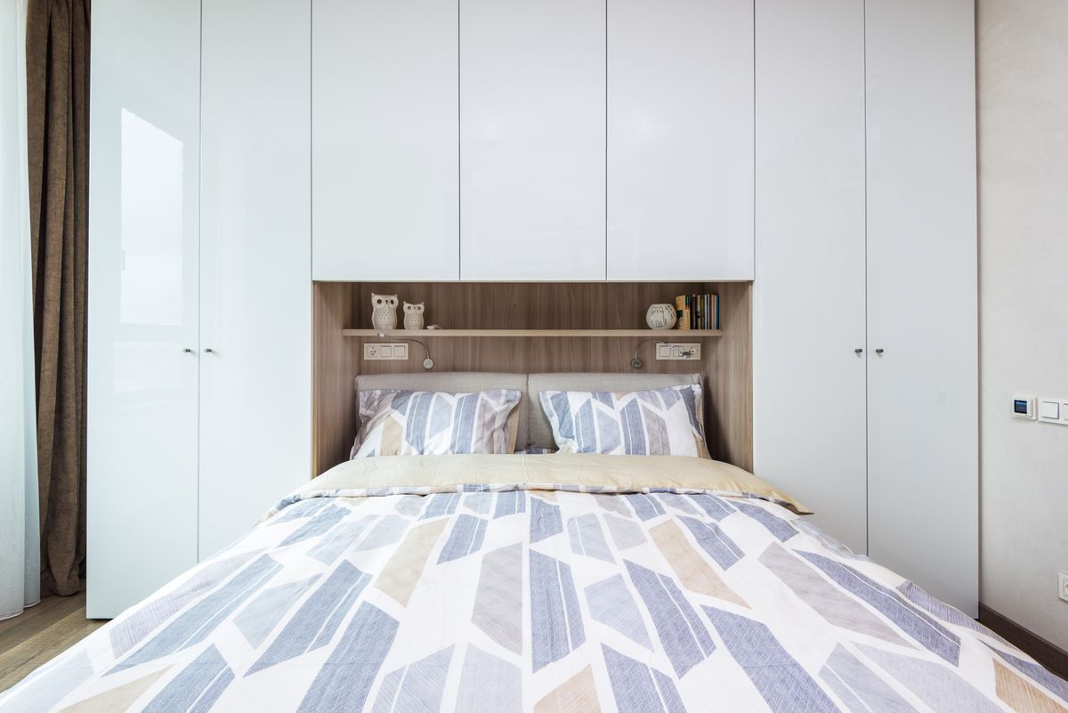 Interior of modern comfortable bedroom with bed with pillows and blanket under shelf combined with bedside wardrobe Interior of modern comfortable bedroom with bed with pillows and blanket under shelf combined with bedside wardrobe