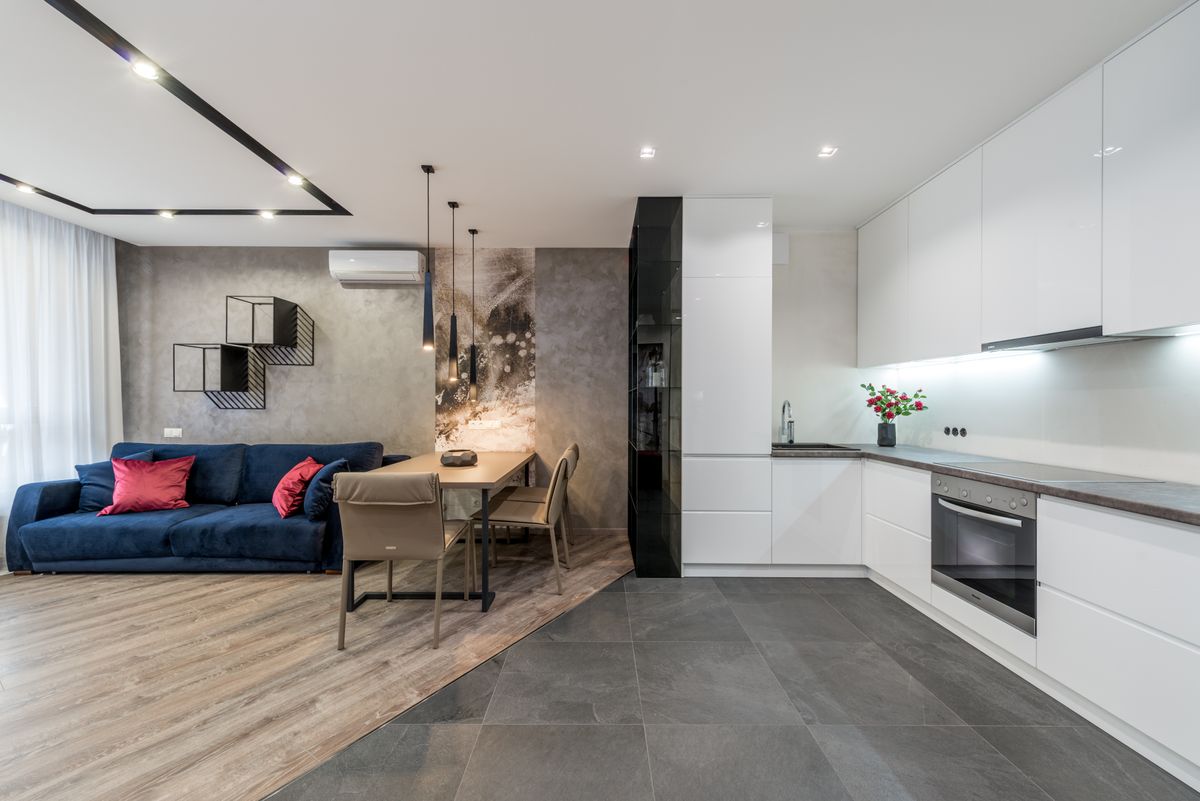 Interior of spacious modern studio apartment with minimalist white furniture in kitchen and comfortable soft sofa in living room