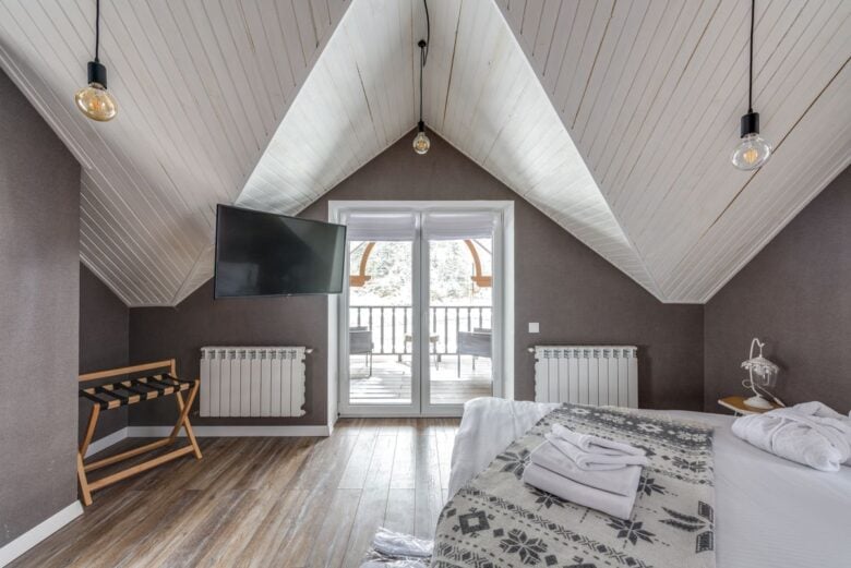 A serene attic bedroom featuring a balcony, TV, and decorative lights.