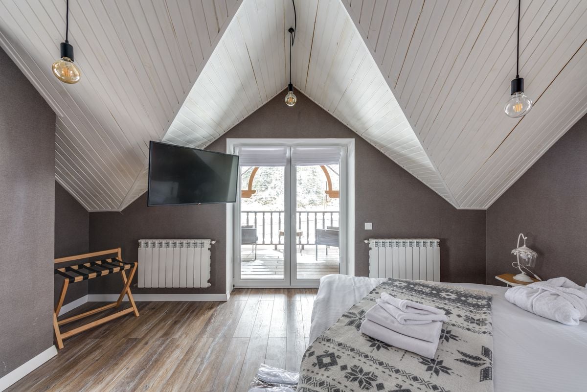 A serene attic bedroom featuring a balcony, TV, and decorative lights. A serene attic bedroom featuring a balcony, TV, and decorative lights.